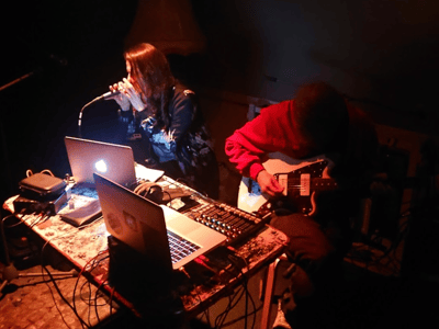 Artists performing live at Madame Claude, combining voice and guitar on stage, captivating the audience in an intimate atmosphere.