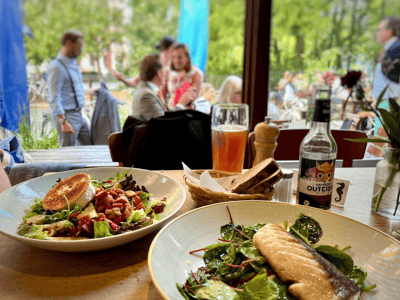 Fresh salad and fish fillet at Strandbad Mitte, with guests in the background enjoying the summer atmosphere.
