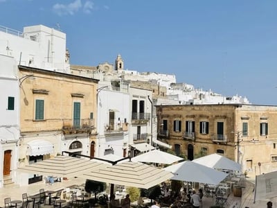 Lively place in Ostuni with terraces, historical buildings, and a blue sky, perfect for enjoying an outdoor coffee.