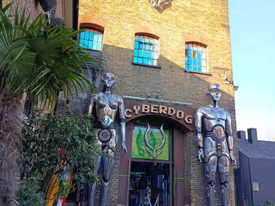 Entrance of the Cyberdog store in London, flanked by futuristic robotic statues and lush vegetation.