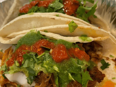 Tacos topped with green and red salsa, fresh cilantro, served at El Mil Sabores, representing Mexican street food.