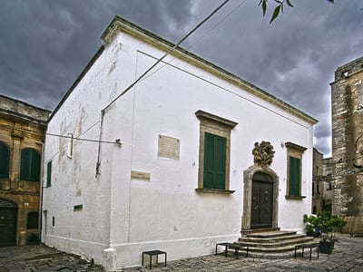 Bishop's Palace and Diocesan Museum in Lecce, with its white architecture and green windows under a cloudy sky.