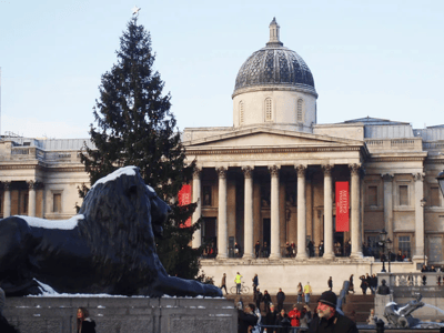 Lion of Trafalgar Square in front of the National Gallery, with a Christmas tree and visitors admiring the classical architecture.