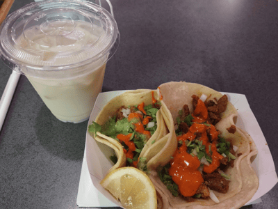 Deux tacos garnis de salsa et guacamole, accompagnés d'un verre de boisson crémeuse, à Eva's x Cinco de Mayo.