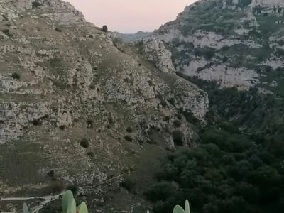 Vue panoramique du Parc Murgia Materana, avec ses collines rocheuses et sa végétation verdoyante au crépuscule.
