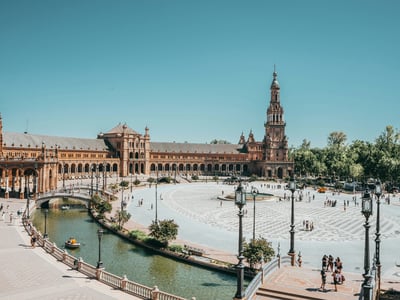 Vue panoramique de la Plaza de España à Séville, avec des visiteurs admirant l'architecture et les canaux environnants.