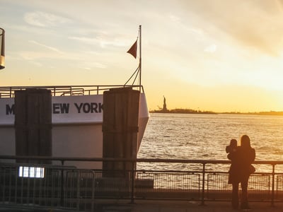 Vue sur la statue de la Liberté au coucher de soleil depuis Battery Park, avec des visiteurs admirant le panorama.