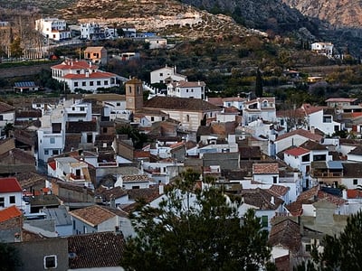 Vue panoramique des toits blancs de Conchàr, surplombés par des montagnes verdoyantes, illustrant le charme pittoresque du village.