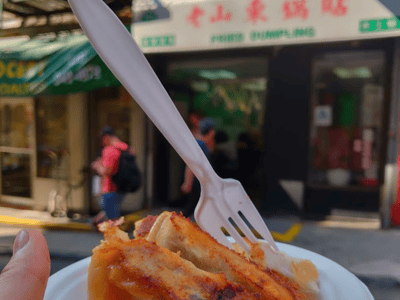 Crispy dumplings from Fried Dumpling, with a fork, in front of the lively display of the restaurant in Chinatown.