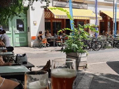 Lively terrace at Strandbad Mitte with customers enjoying drinks, surrounded by greenery and parked bikes.