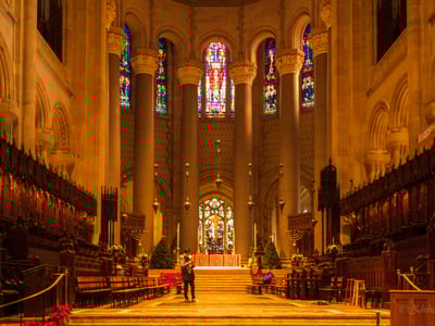 Interior of St John the Divine Cathedral, showcasing colorful stained glass windows and majestic stone pillars.