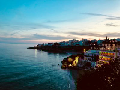Coucher de soleil sur la côte de Nerja, illuminant les maisons emblématiques et la mer calme.