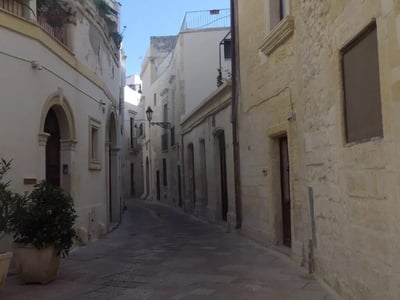 Rue pavée à Lecce, flanquée d'imposants bâtiments historiques et de balcons fleuris en apalte. Un charme méditerranéen.