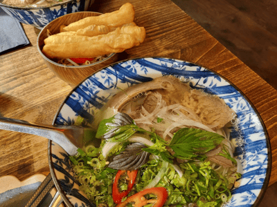 Bol de phở aromatique avec des herbes fraîches et des tranches de viande, accompagné de beignets à PHO - Noodlebar.