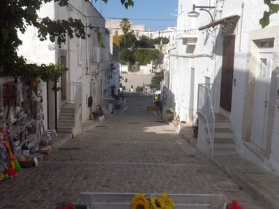 Rue pavée du Quartier Monti, ornée de fleurs, avec des maisons blanches typiques et une ambiance méditerranéenne paisible.