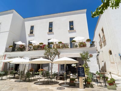 Sunny terrace of Palazzo Indelli, with white umbrellas and colorful flowers, offering a relaxing atmosphere in Ostuni.