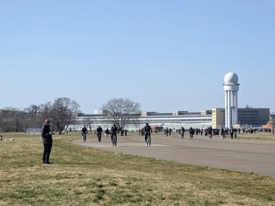 Cyclists and walkers enjoy the vast space of Tempelhofer Feld, with its historic buildings in the background.