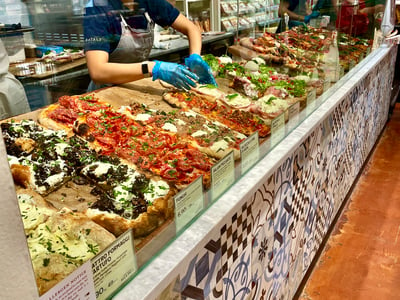 Variety of fresh pizzas displayed at a counter in Eataly New York, illustrating Italian culinary art.