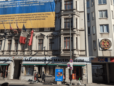 Museum shop at the Berlin Wall, with flags and a large banner on rights in Ukraine, symbolizing history and commitment.