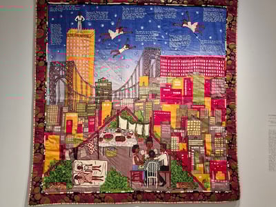 Colorful quilt representing a vibrant urban scene, displayed at the Barbican Art Gallery, blending culture and contemporary art.