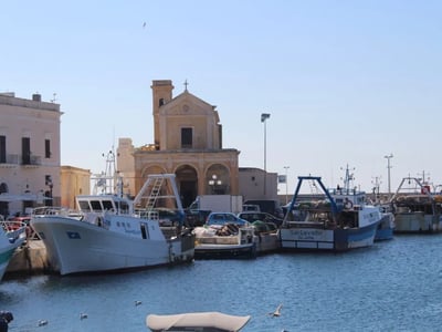 Old boats moored at the Port of Gallipoli, with the historic church in the background, evoking the local maritime history.
