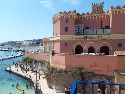 View of Tricase Porto, highlighting a historic building with visitors enjoying the sun and the sea.