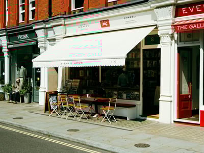 Newsstand in Marylebone, with an outdoor terrace and wooden chairs, offering newspapers and magazines.