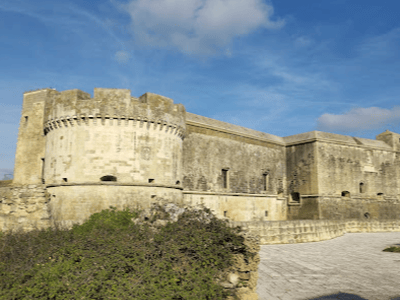 Vue du Château d'Acaya, forteresse historique du XVIe siècle, entourée de paysages pittoresques et de ciel bleu.