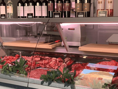 Showcase of the Macelleria Perricci with fresh meats and a selection of fine wines in the background.
