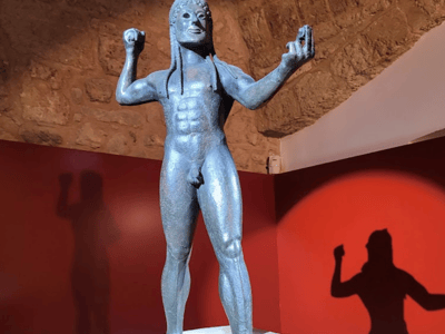 Bronze statue of a young man standing at the New Archaeological Museum, illustrating ancient art.