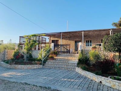 Stone house in Mare Chiaro, with a beautiful terrace, surrounded by flowering gardens and a clear blue sky.