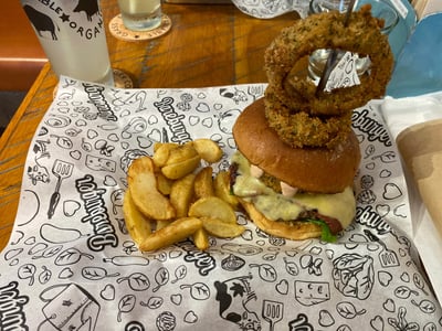 Burger topped with cheese, crispy onion rings, and fries, served at Bare Burger.