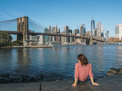 View from the Brooklyn Bridge with a woman contemplating the New York skyline and the calm water at her feet.