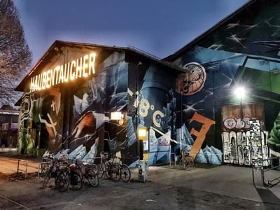 Mur de graffiti coloré sur le bâtiment du RAW-Gelände, illuminé par des néons, avec des vélos stationnés à l'avant.