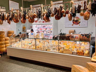 Selection of cheeses and cured meats hanging at the counter of Eataly New York, highlighting Italian cuisine.