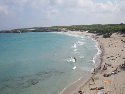Torre dell'Orso beach with bathers, a partially cloudy sky, and lush dunes in the background.