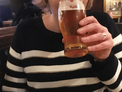 Woman wearing a black and white striped sweater, enjoying a beer in the friendly atmosphere of the Punch Tavern in London.