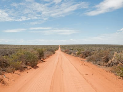 Une route de terre rouge menant à travers le paysage sauvage près d'Exmouth, symbolisant les aventures en plein air.