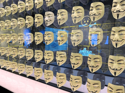 Masques emblématiques suspendus, symbolisant l'anonymat et la révolte, exposés au musée Spyscape à New York.