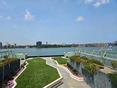 Panoramic view of the park on the roof of Pier 57, with green spaces and a view of the Hudson River and Manhattan.