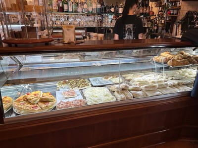 Showcase of La bottega de I Pastini, displaying pieces of Italian pastries, with a friendly atmosphere in the background.