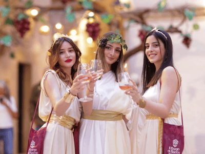 Trois femmes en toges blanches, levant des verres, célébrant lors de Cortili Aperti, ambiance festive et conviviale.