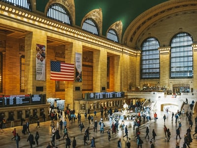 Crowd of people in the monumental hall of Grand Central Station, with American flag and display boards.