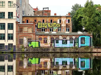 Graffiti coloré sur des bâtiments historiques au bord d'un canal à Kreuzberg, reflet dans l'eau créant une ambiance urbaine vivante.