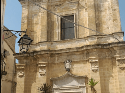 Historic church in Castellaneta, with a stone facade featuring refined architectural details and palm trees in front of the entrance.