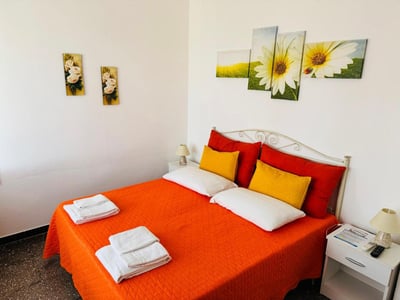 Bright room in Mare Chiaro with an orange bed, yellow pillows, and soothing floral decor. Perfect for relaxing.