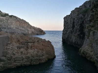 Impressive rocks framing a calm cove at Il Ciolo, creating a picturesque natural setting by the sea.