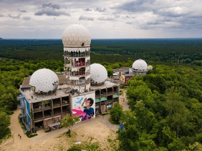 Ruins of the listening station on Teufelsberg, with domes and a colorful mural, surrounded by lush nature.