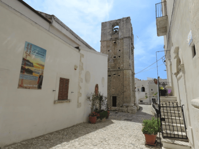 View of the bell tower of St. Elias Church, surrounded by cobblestone streets and Mediterranean vegetation.