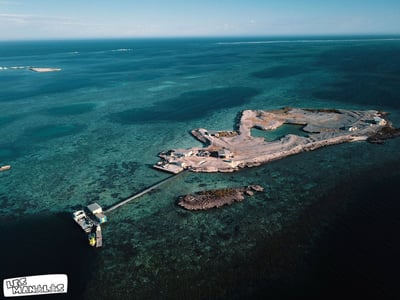 Aerial view of the Abrolhos Islands, illustrating a turquoise lagoon surrounded by coral reefs and a pier.